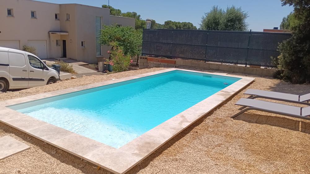 Piscine rectangulaire terminée, margelles en travertin et plage de gravier